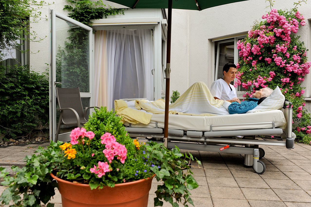Pflegerin der Palliativstation sitzt draußen am Bett der Patientin