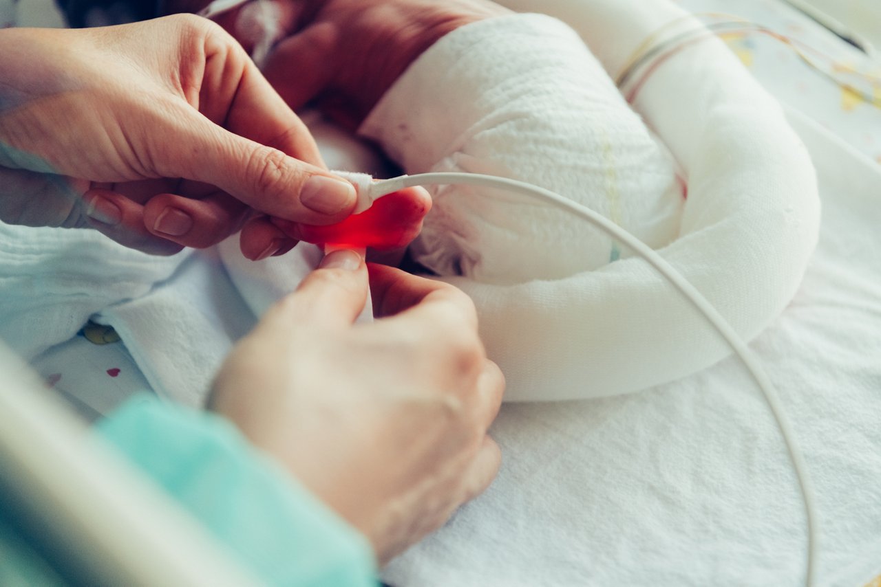 Hände befestigen vorsichtig ein Kabel am Fuß des Frühchens