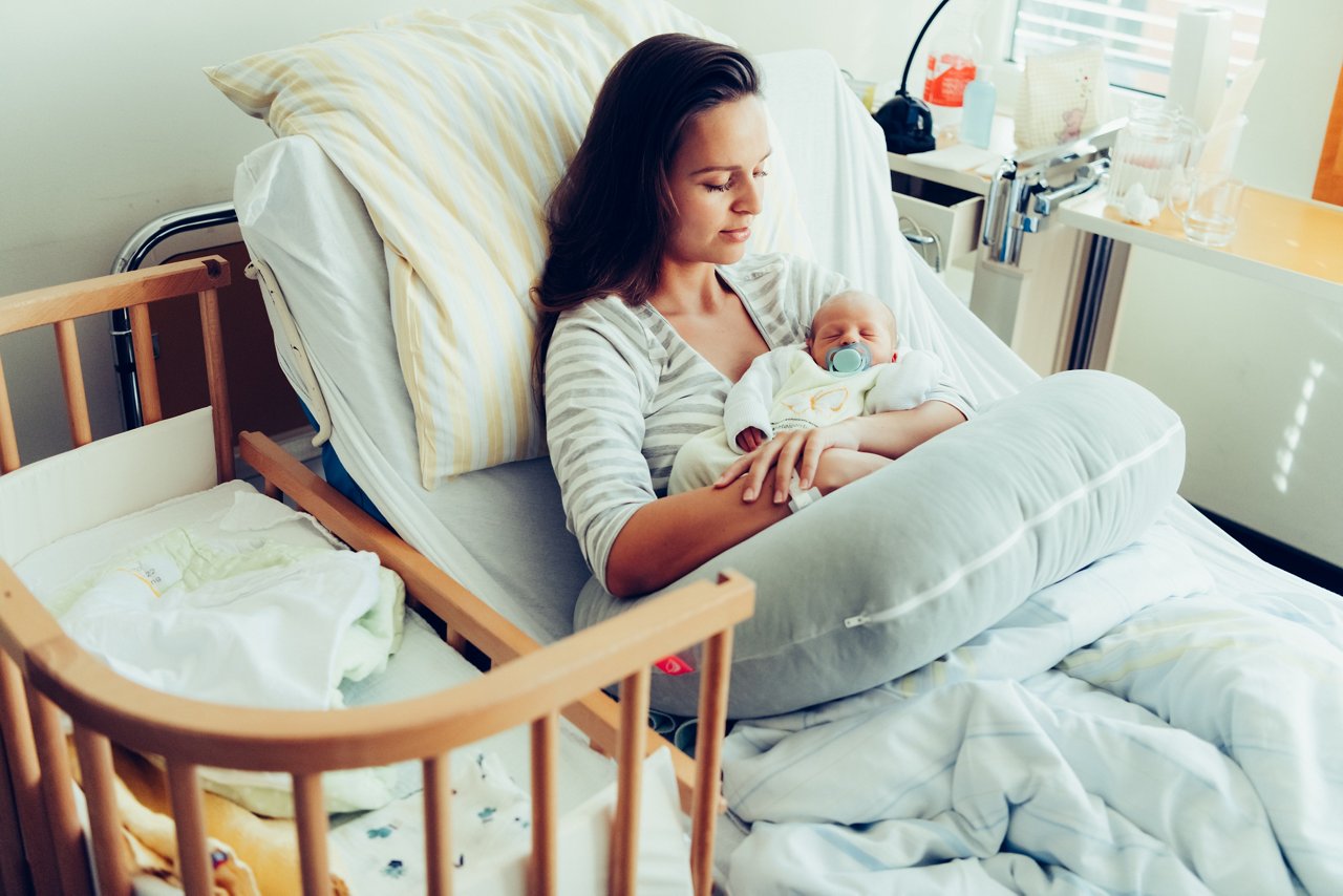 Mutter liegt im Bett und hält ihr Baby im Arm