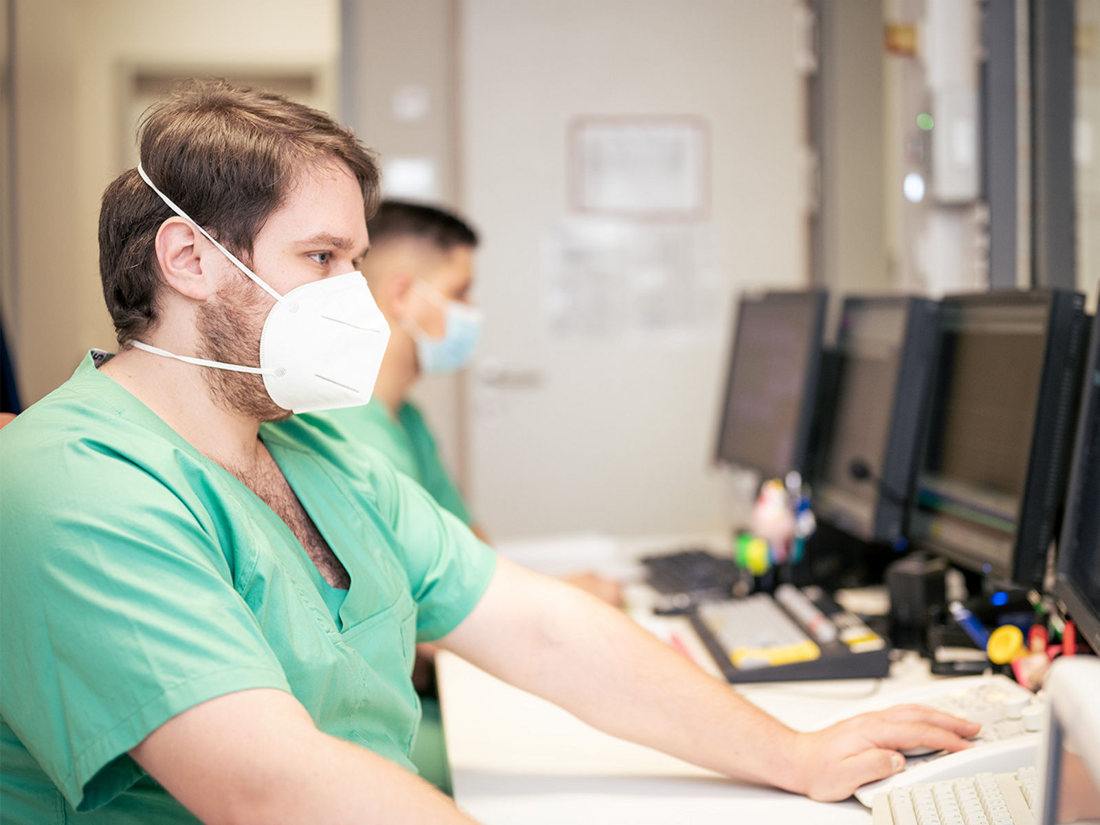 Ein Kardiologe mit Maske arbeitet an einem Computer