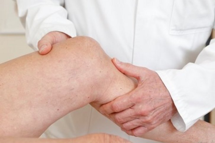Arzt berührt nacktes Bein eines Patienten oder einer Patientin in Höhe des Knies