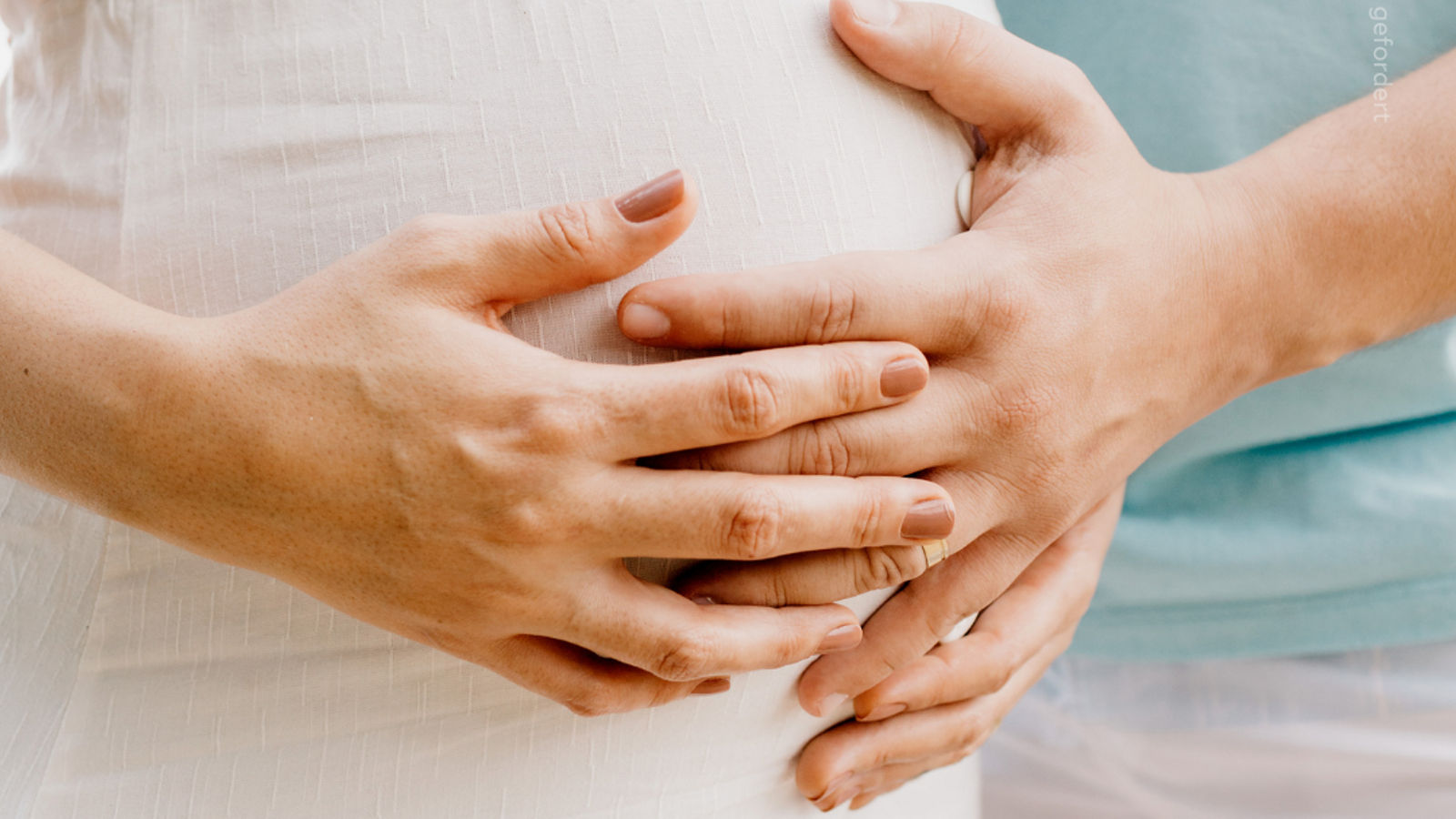 Eine Schwangere und Ihr Partner legen ihre Hände auf den Schwangerschaftsbauch.