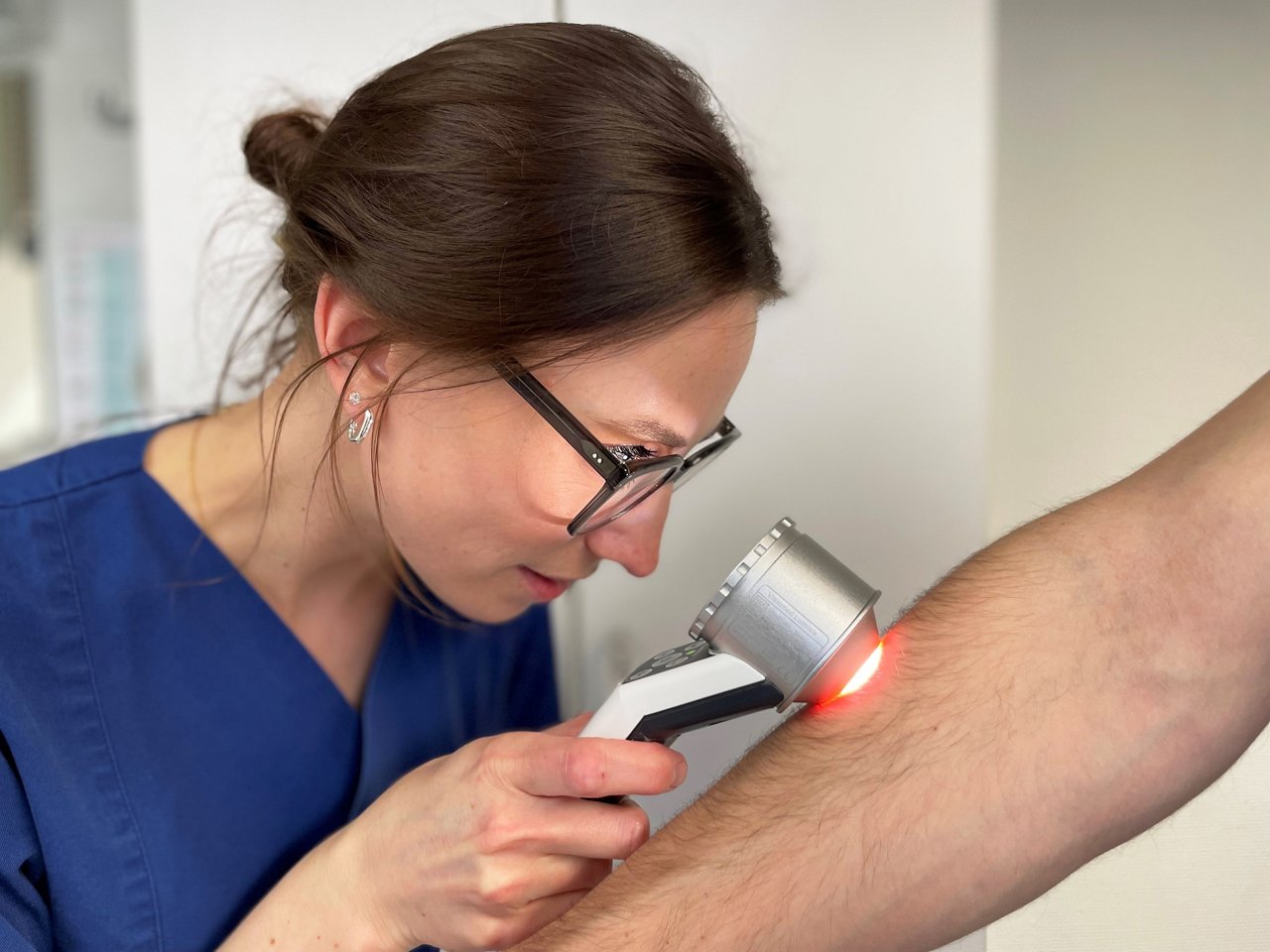 Dermatologin untersucht Arm mit Dermatoskop