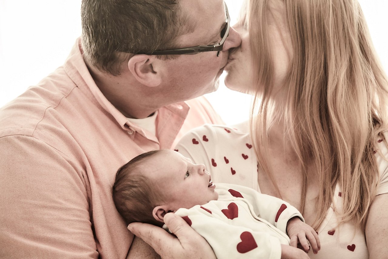 Eltern kuessen mit Baby im Arm