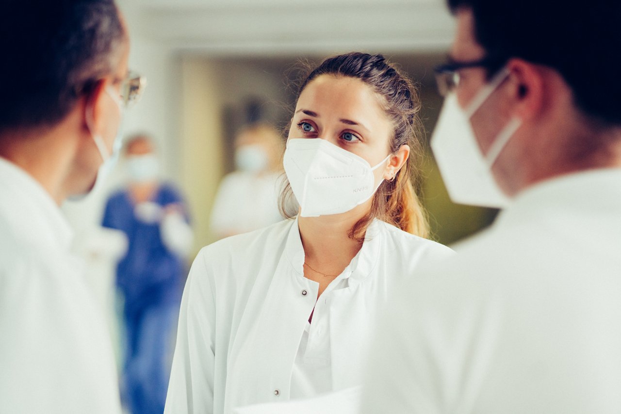 Personen in ärztlicher Bekleidung mit FFP2 Masken stehen gemeinsam zusammen und beraten