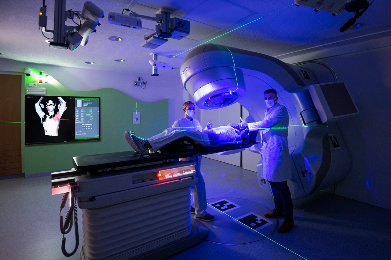 Chefarzt Prof. Piroth am Bestrahlungsgerät mit einer Mitarbeiterin und Patientin