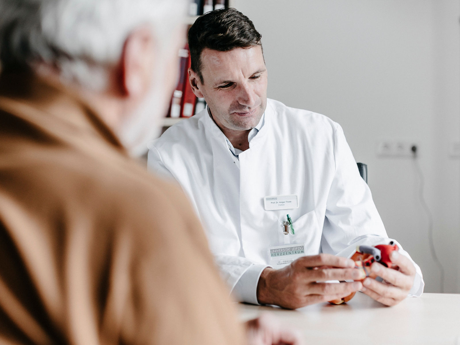 Ein Arzt erklärt einem älteren Patienten anschaulich medizinische Informationen mit einem Modell. Die vertrauensvolle Atmosphäre fördert das Verständnis und die Kommunikation.