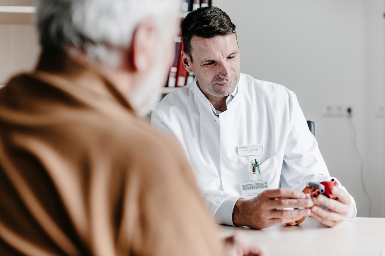 Ein Arzt erklärt einem älteren Patienten anschaulich medizinische Informationen mit einem Modell. Die vertrauensvolle Atmosphäre fördert das Verständnis und die Kommunikation.