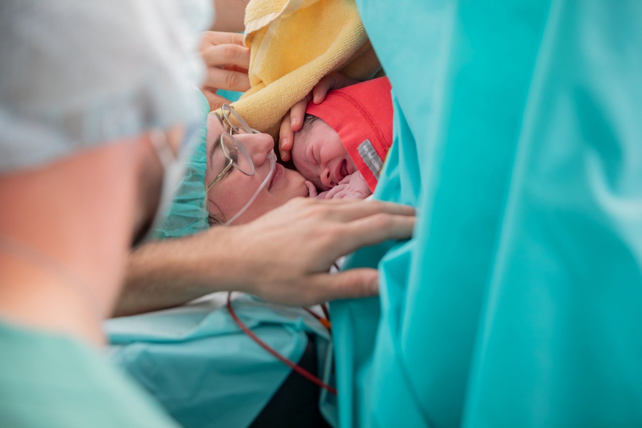 Baby kurz nach Kaiserschnitt im Bondingtuch bei seiner Familie