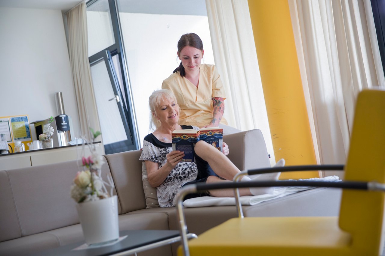Pflegerin und Patientin schauen gemeinsam in ein Buch