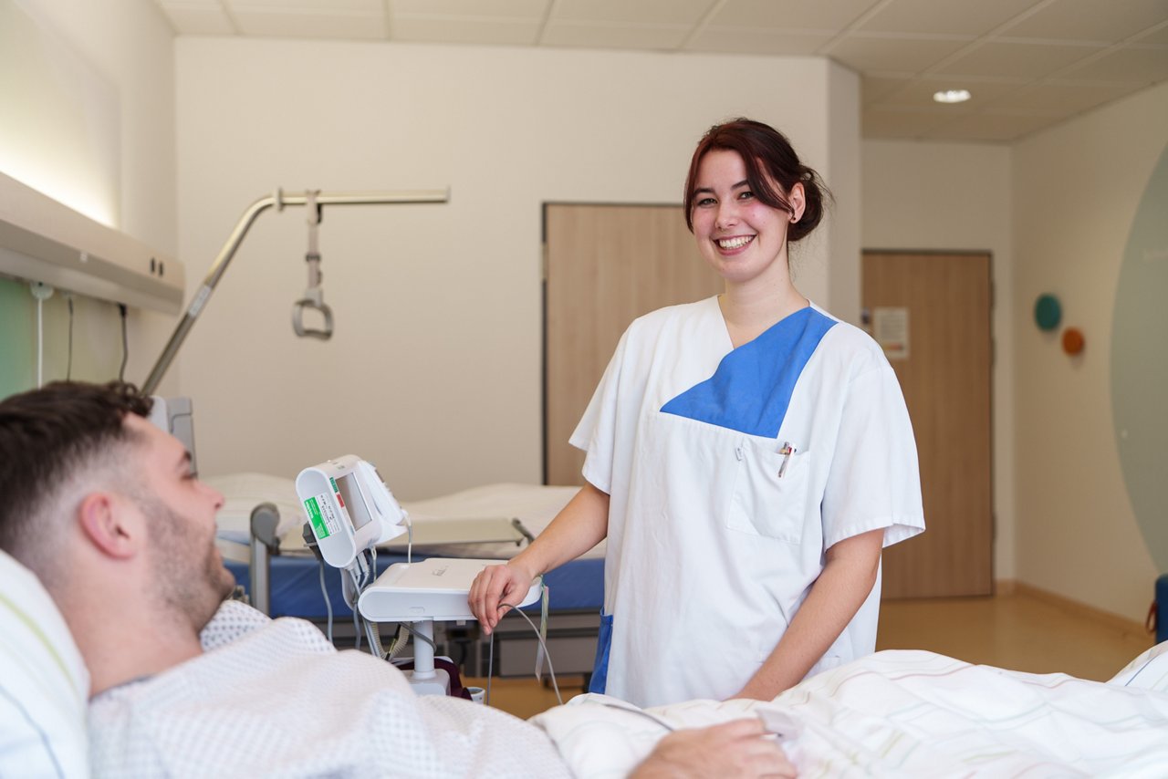 Auszubildende versorgt Patienten und lächelt dabei in die Kamera
