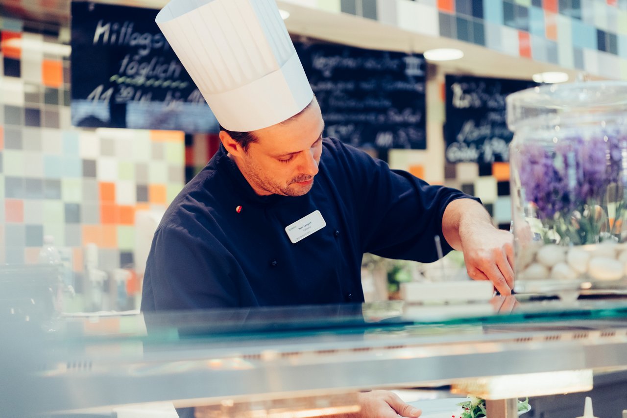 Koch hinter der Theke tut Essen auf einen Teller auf