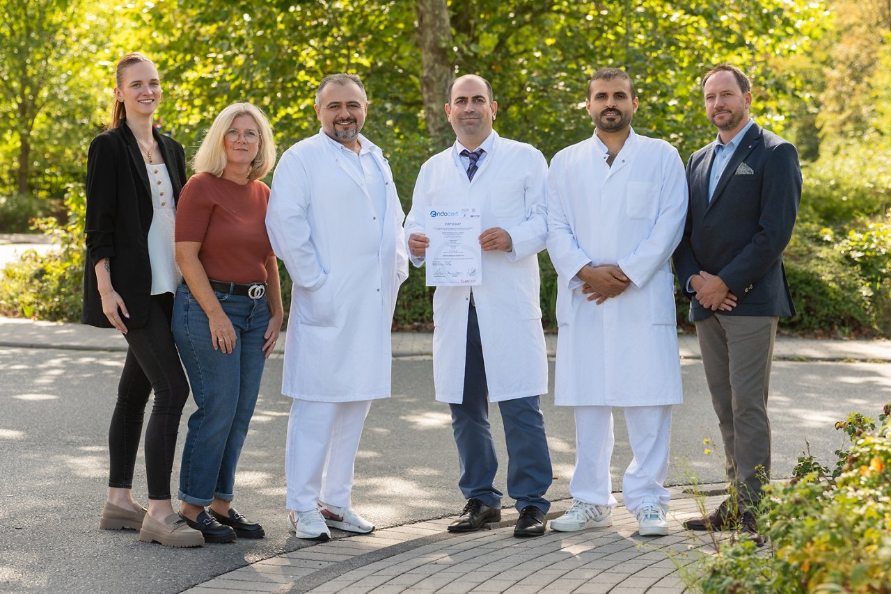 Ein Team von Fachleuten in weißen Kitteln steht im Freien und präsentiert stolz ein Zertifikat. Sie repräsentieren Expertise und Engagement in der Gesundheitsversorgung.
