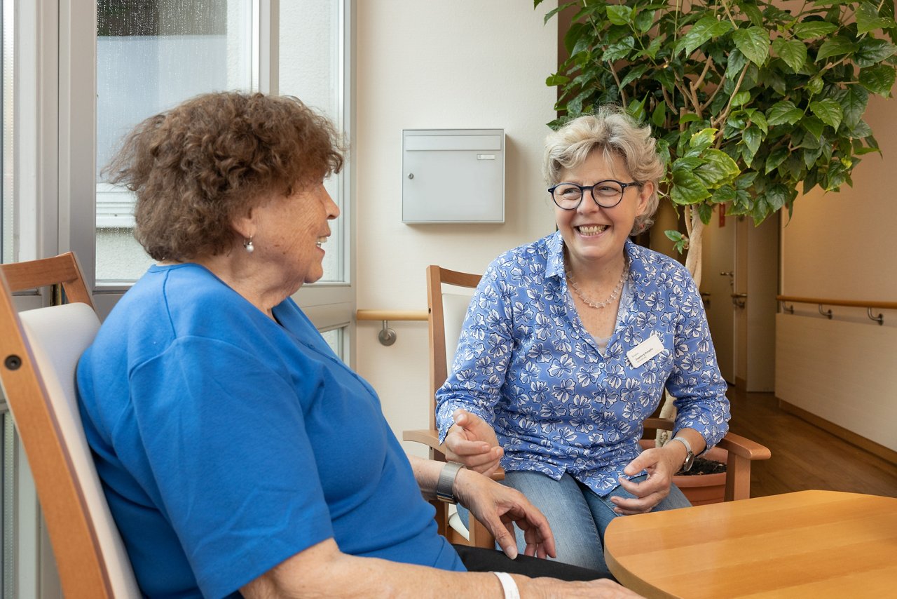 Ehrenamtliche und Patientin sitzend am Tisch im Gespräch