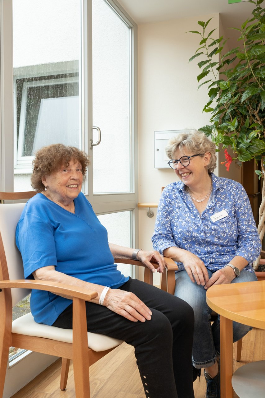 Ehrenamtliche und Patientin sitzend am Tisch im Gespräch