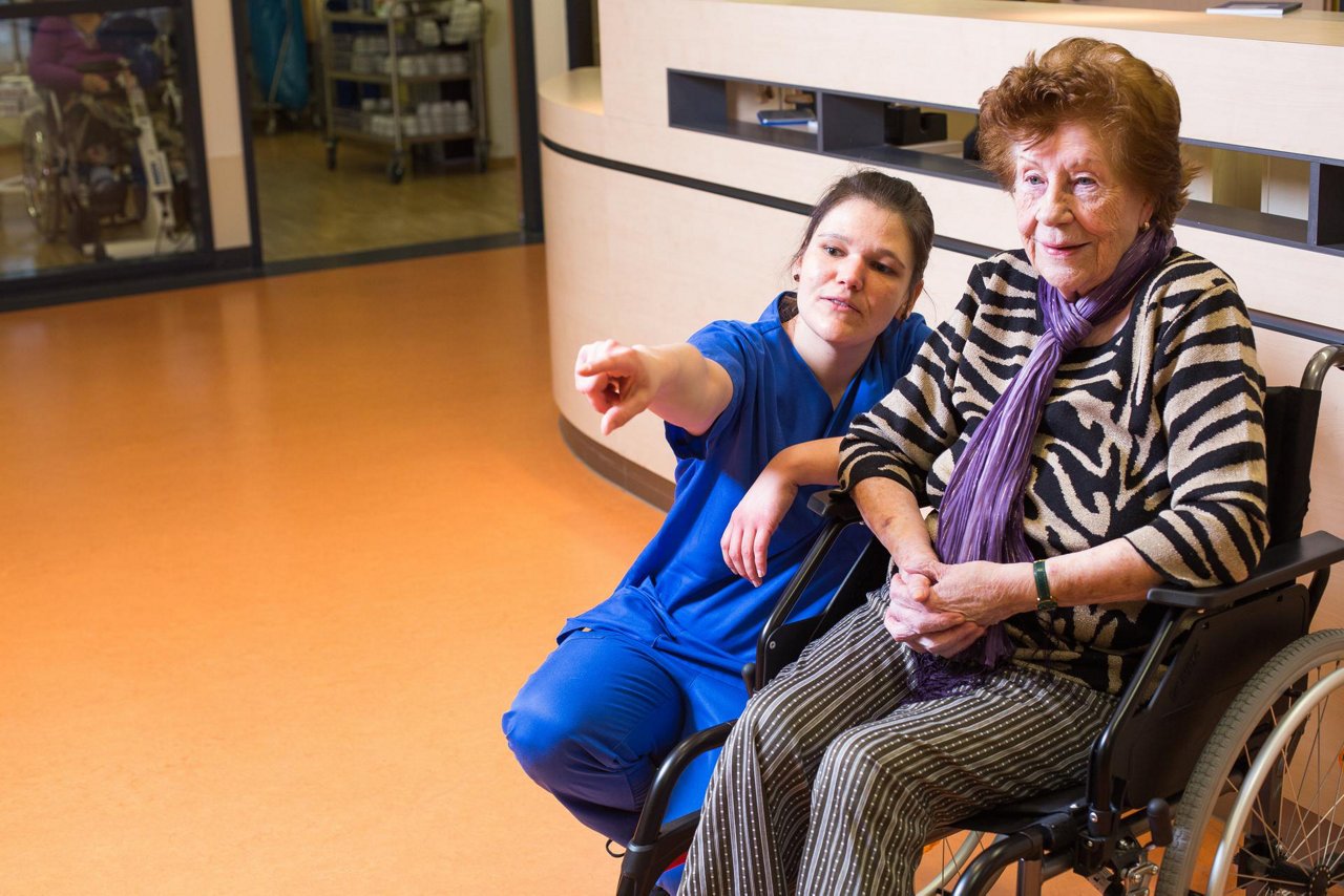 Pflege im Gespräch mit Patient in der Geriatrie am Stationstresen