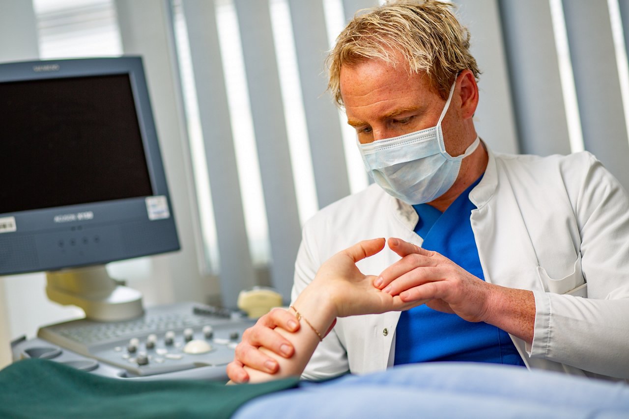 Oberarzt untersucht die Hand einer Patientin