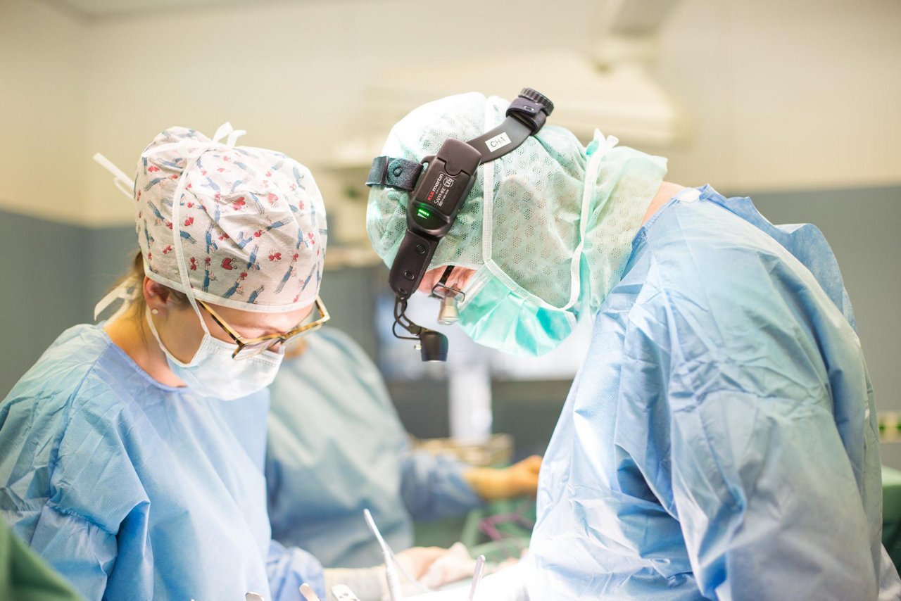 Operateur operiert mit Lupenbrille und wird von einer Operateurin unterstützt