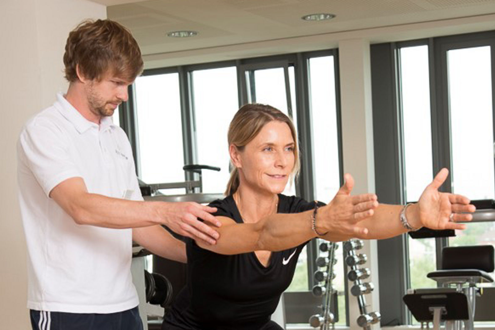 Physiotehrapie Training Kniebeuge Therapeut und Patientin mit ausgestreckten Armen