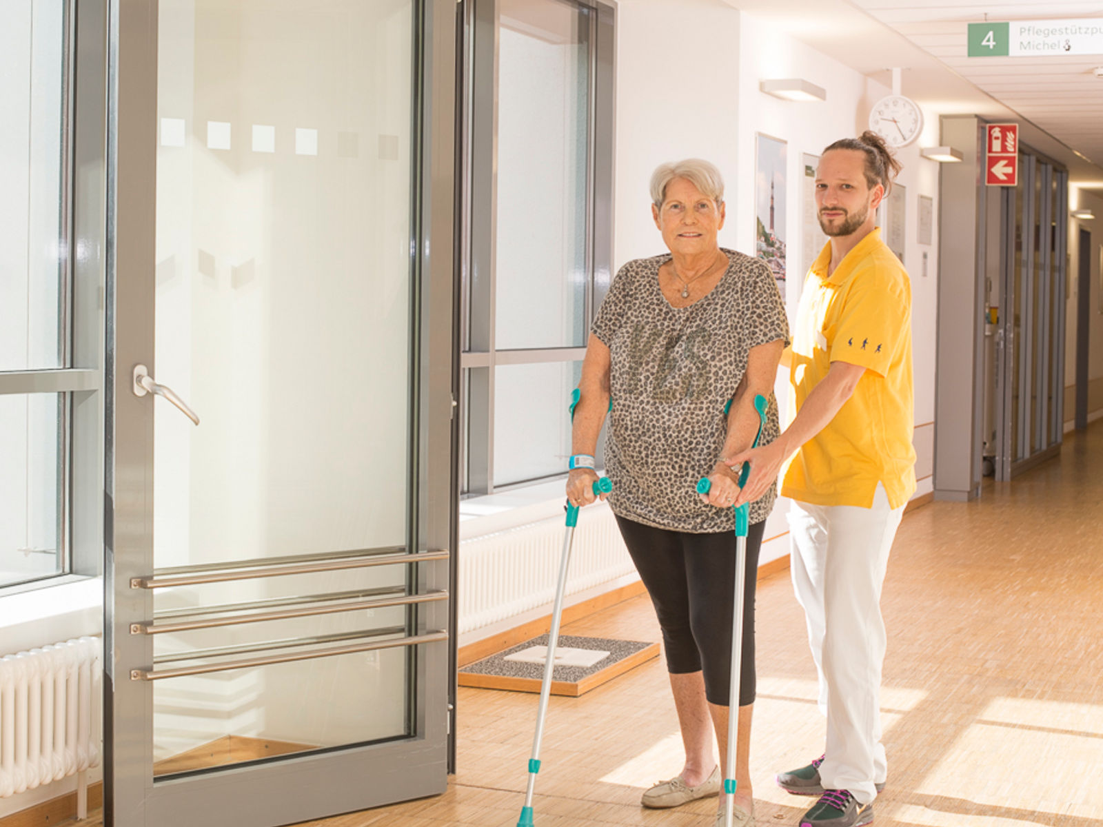 Ein Physiotherapeut zeigt einer Patientin wie sie auf Krüken läuft