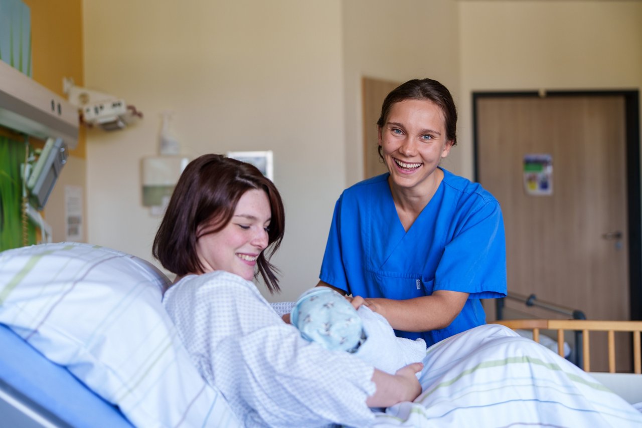 Pflegerin sieht nach ihren Patienten in der Geburtshilfe und lächelt in die Kamera