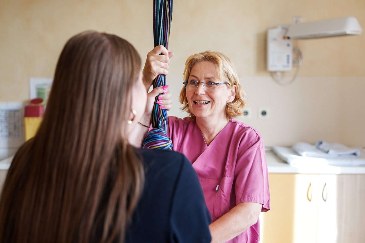 Hebamme hält das von der Decke hängende Tuch im Kreißsaal zusammen mit der Patienten in der Hand und erklärt ihr dies im Zusammenhang mit dem Geburtsvorgang