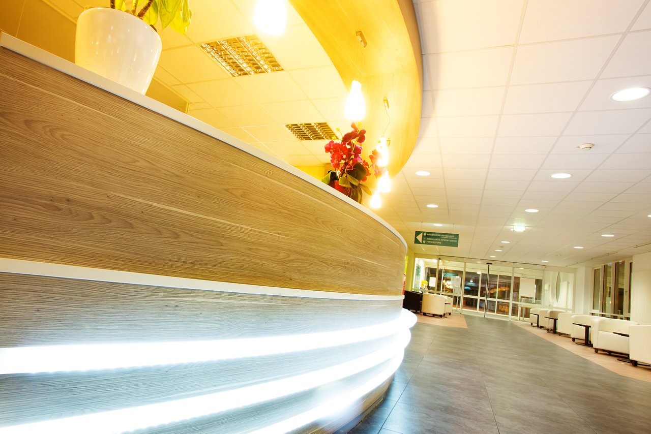 Blick an beleuchtetem Rezeptionstresen vorbei auf Eingangsbereich der Klinik