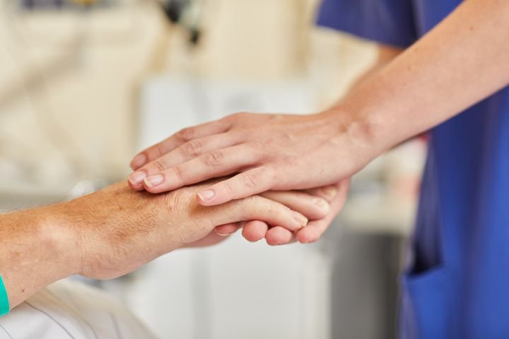  Nahaufnahme: Pflegekraft in Kasack umfasst Hand eines Patienten