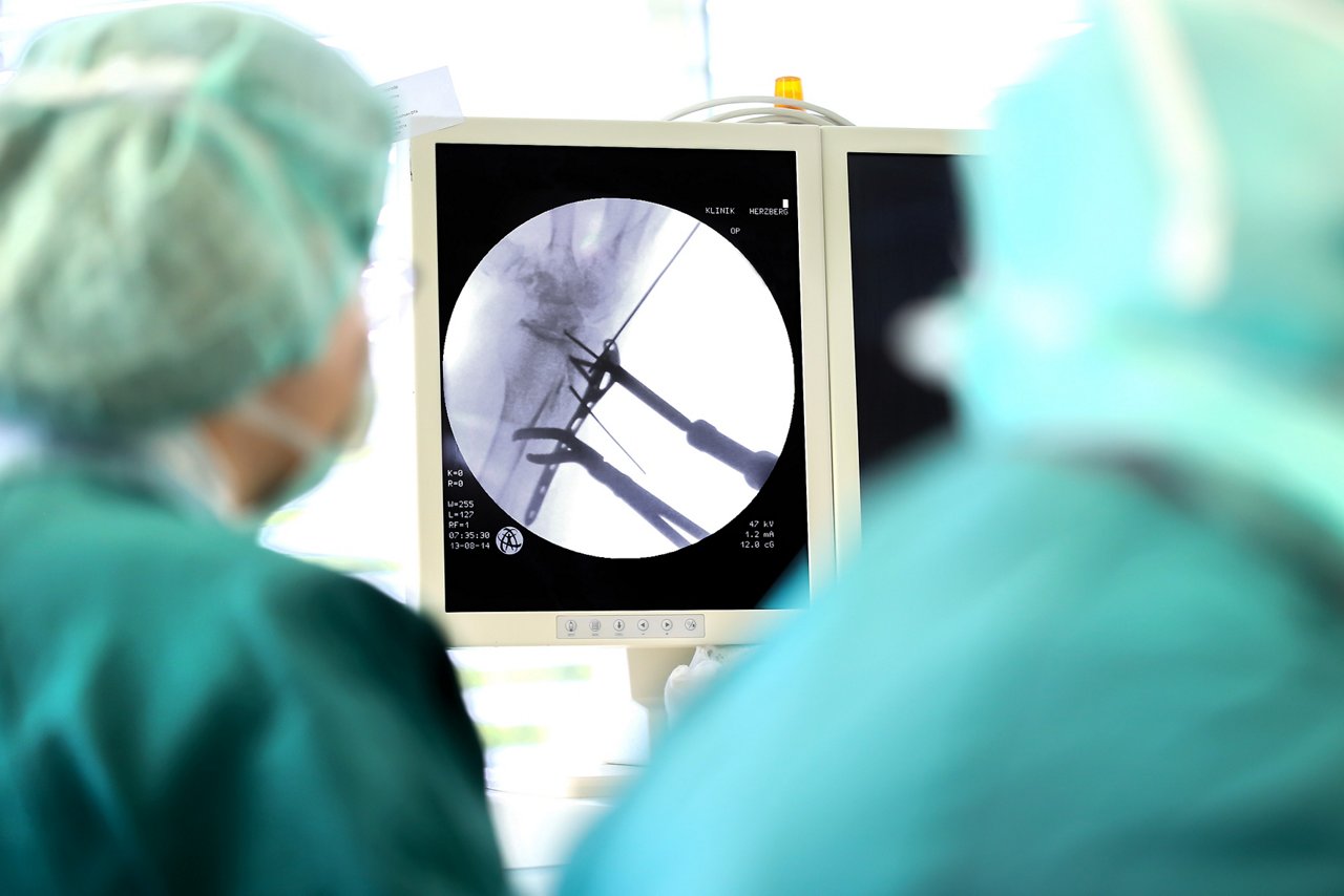 Blick vorbei an zwei Menschen in OP-Kleidung auf Monitor, der Ausschnitt aus Kamera des OP-Geschehens zeigt