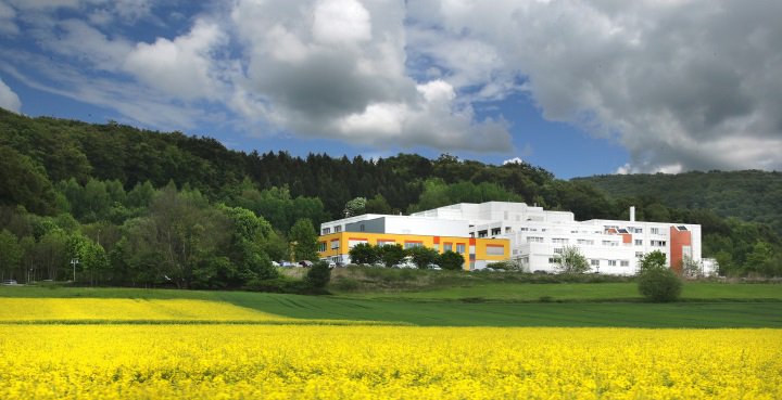 Rapsfeld im Vordergrund, im Hintergrund vor grünem Wald das Klinikgebäude
