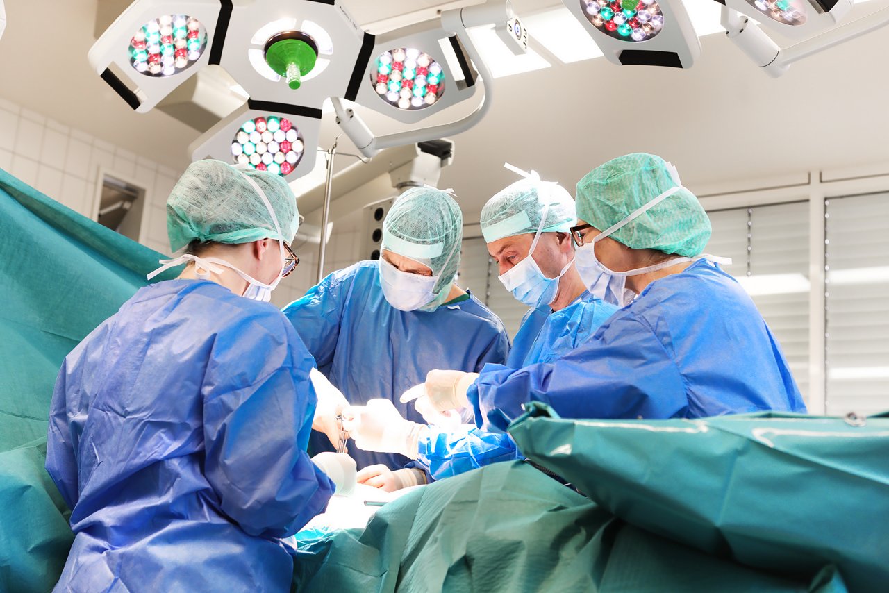 vier Menschen in OP-kleidung stehen um abgedeckten Patienten auf OP-Tisch