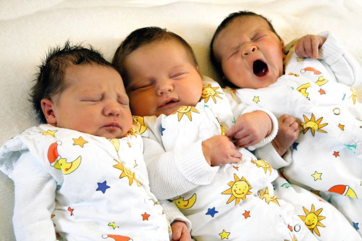 drei schlafende, teils gähnende Babys liegen nebeneinander auf weißer Matratze