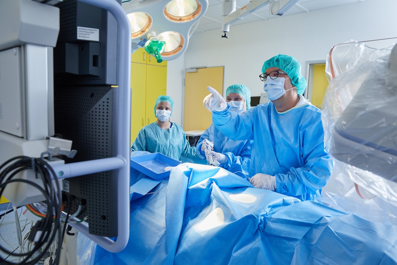  Arzt in OP-Kleidung zeigt während einer OP auf einen Monitor