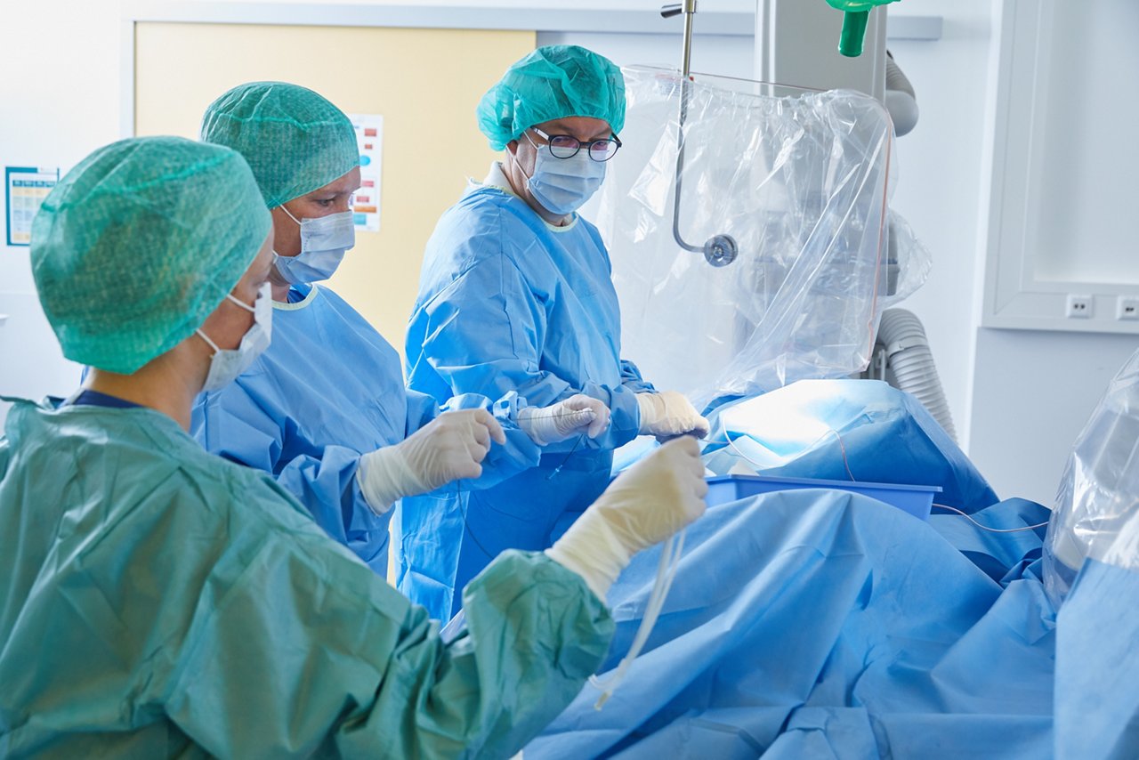  Drei Menschen in OP-Kleidung bei einer Herzkatheteruntersuchung