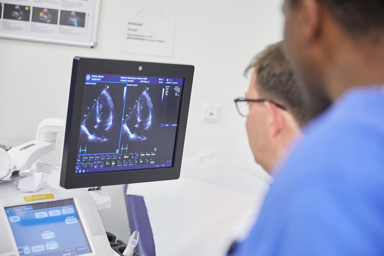  Zwei Männer schauen auf Monitor, der ein Herz-Echo abbildet