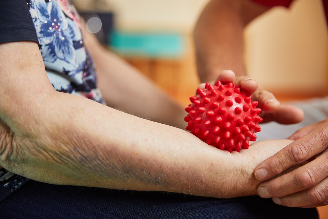  roter Igelball wird über den Unterarm einer älteren Patientin gerollt