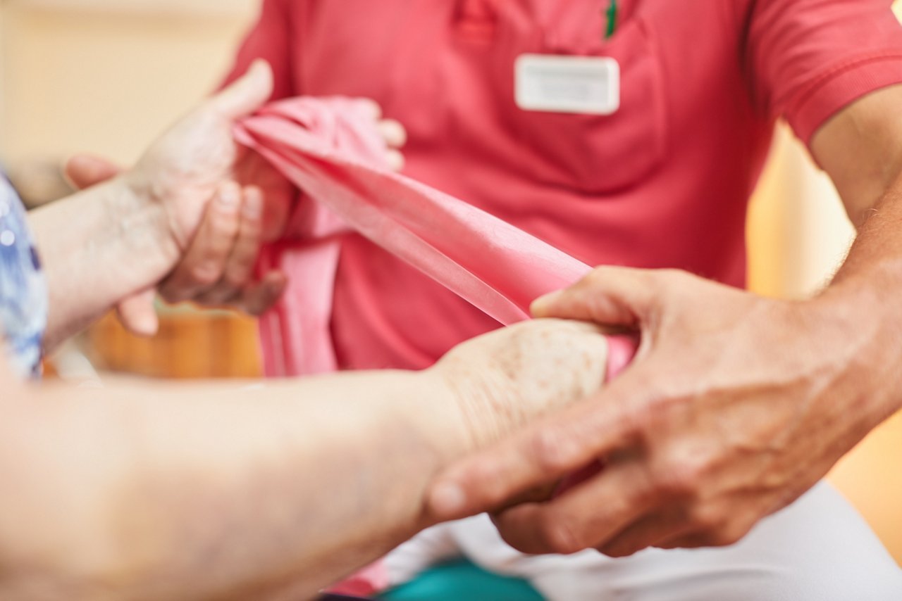  Detailaufnahme eines Physiotherapeuten, der älteren Frau in Benutzung eines Gymnastikbandes anweist