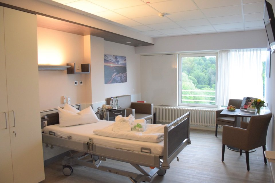 Blick in Patientenzimmer mit einem Bett, Tisch mit Stühlen und Sofa