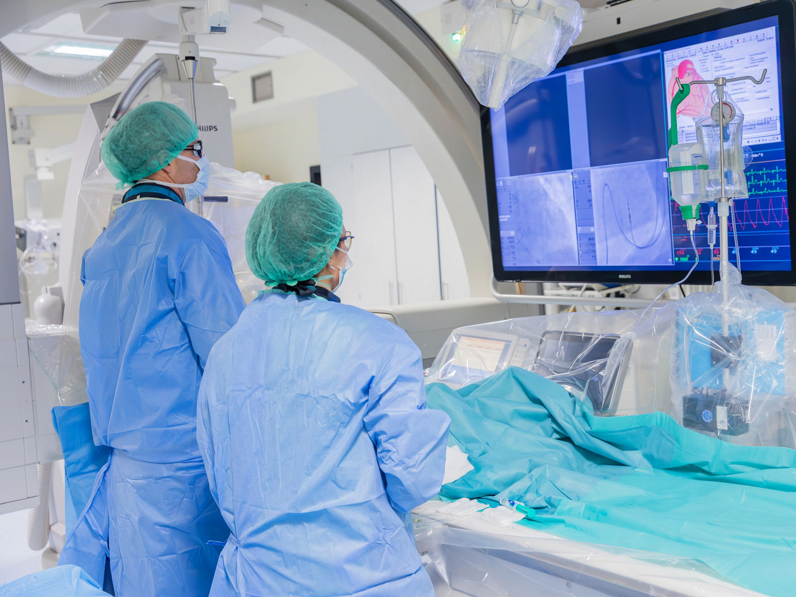 Ärzte in einem modernen Operationssaal betrachten Bildschirme während einer Herzuntersuchung. Die hochmoderne Technologie unterstützt präzise Diagnosen und Behandlungen.