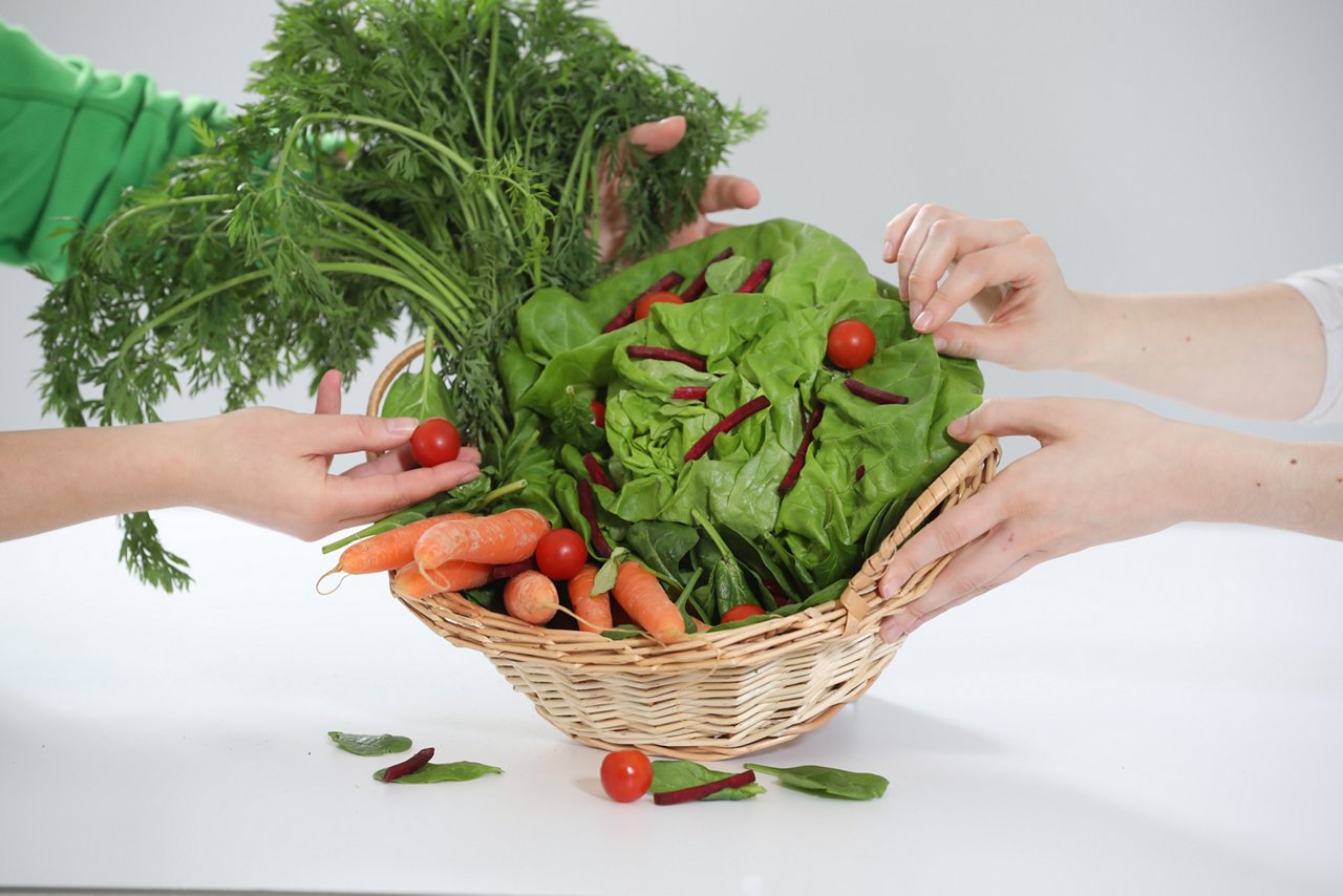 Gemüsekorb mit Salat, Möhren, Tomaten und rote Beete, der von vier Händen gehalten wird.