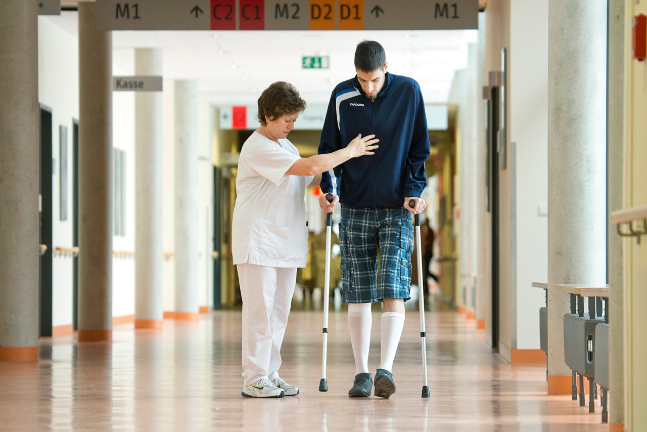 Patient an Gehstützen in Begleitung von Fachpersonal