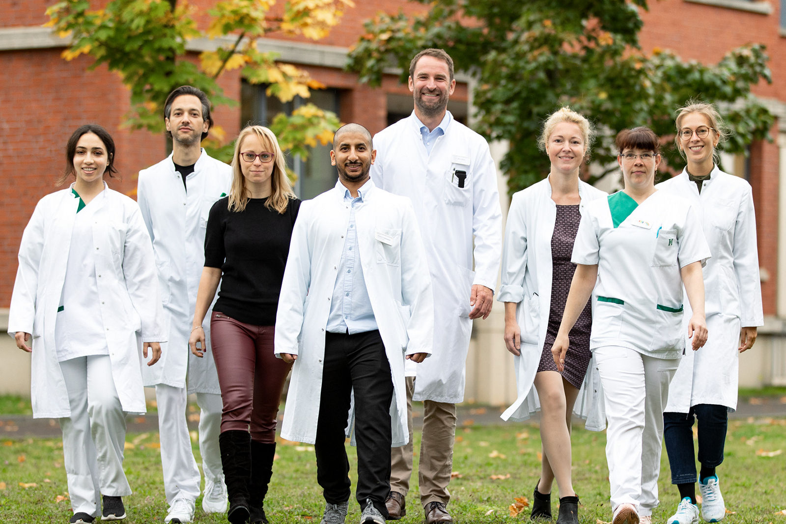 Teammitglieder der plastischen Chirurgie laufen über grüne Wiese vor dem Gebäude des Helios Klinikums Berlin-Buch