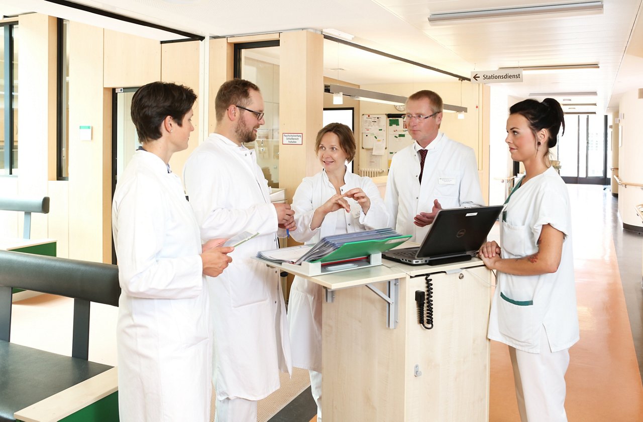 ärztliche und pflegerische Visite auf der Tumororthopädie Fachpersonal steht um den Visitenwagen herum mit aufgeschlagenen Patientenakten und Laptop