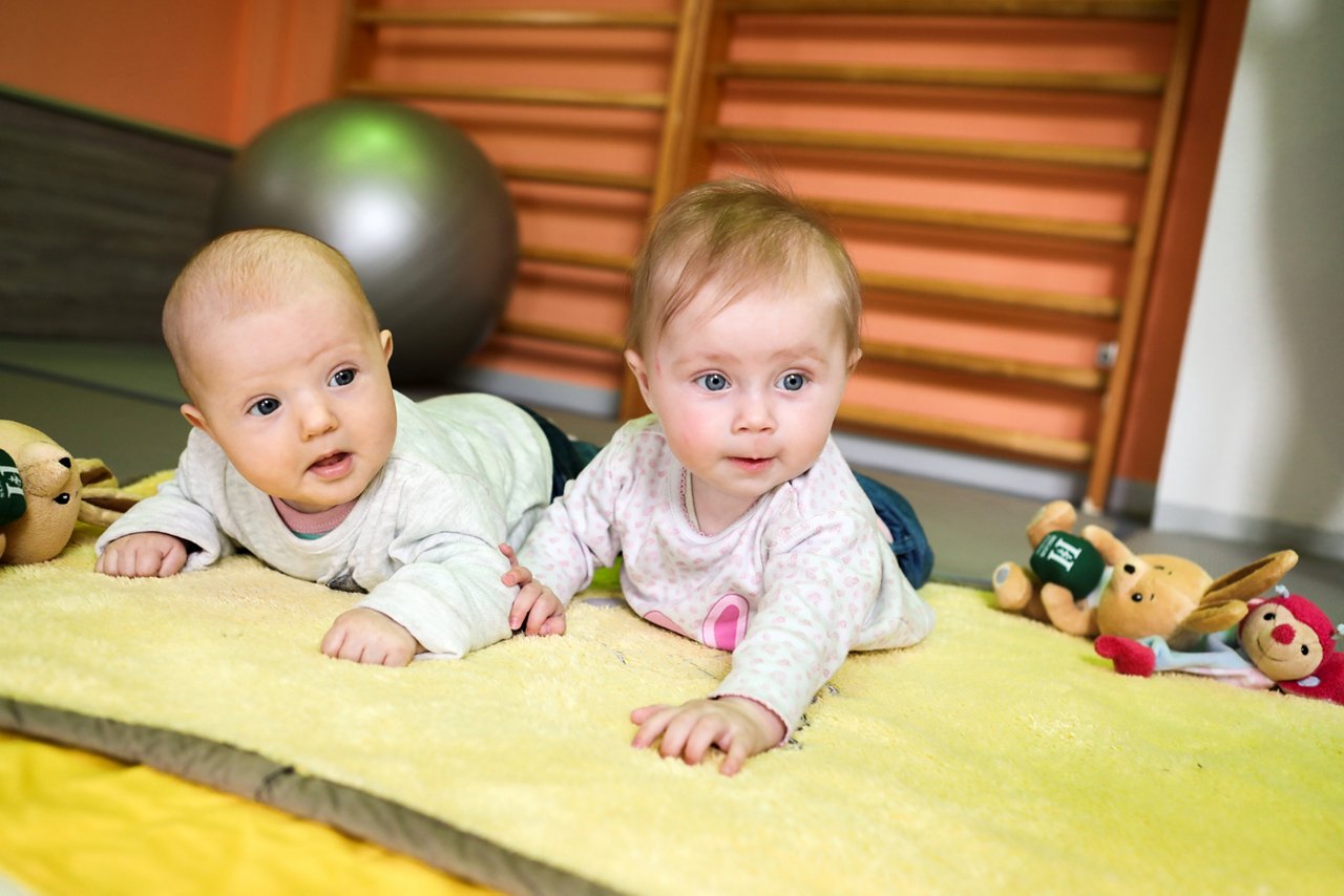 Auf dem Bauch liegende Babys bei der Elternschule schauen in die Kamera 