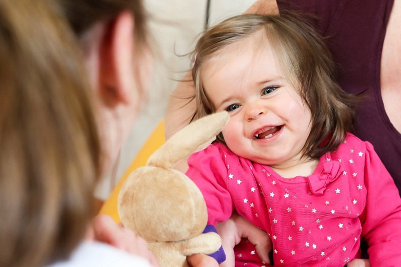Nahaufnahme eines lachenden Kleinkindes auf dem Schoß seiner Mutter