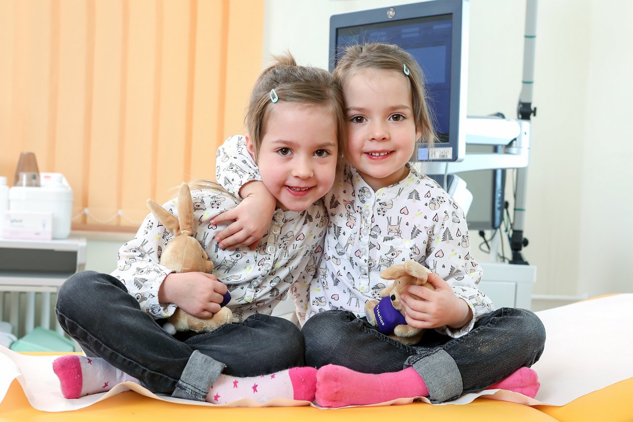 Foto von zwei Zwillingen die auf eine Liege sitzen und auf eine Untersuchung warten
