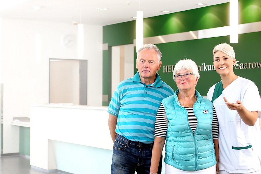 Zwei Patienten werden am Empfangstresen von einer Schwester der Klinik begleitet