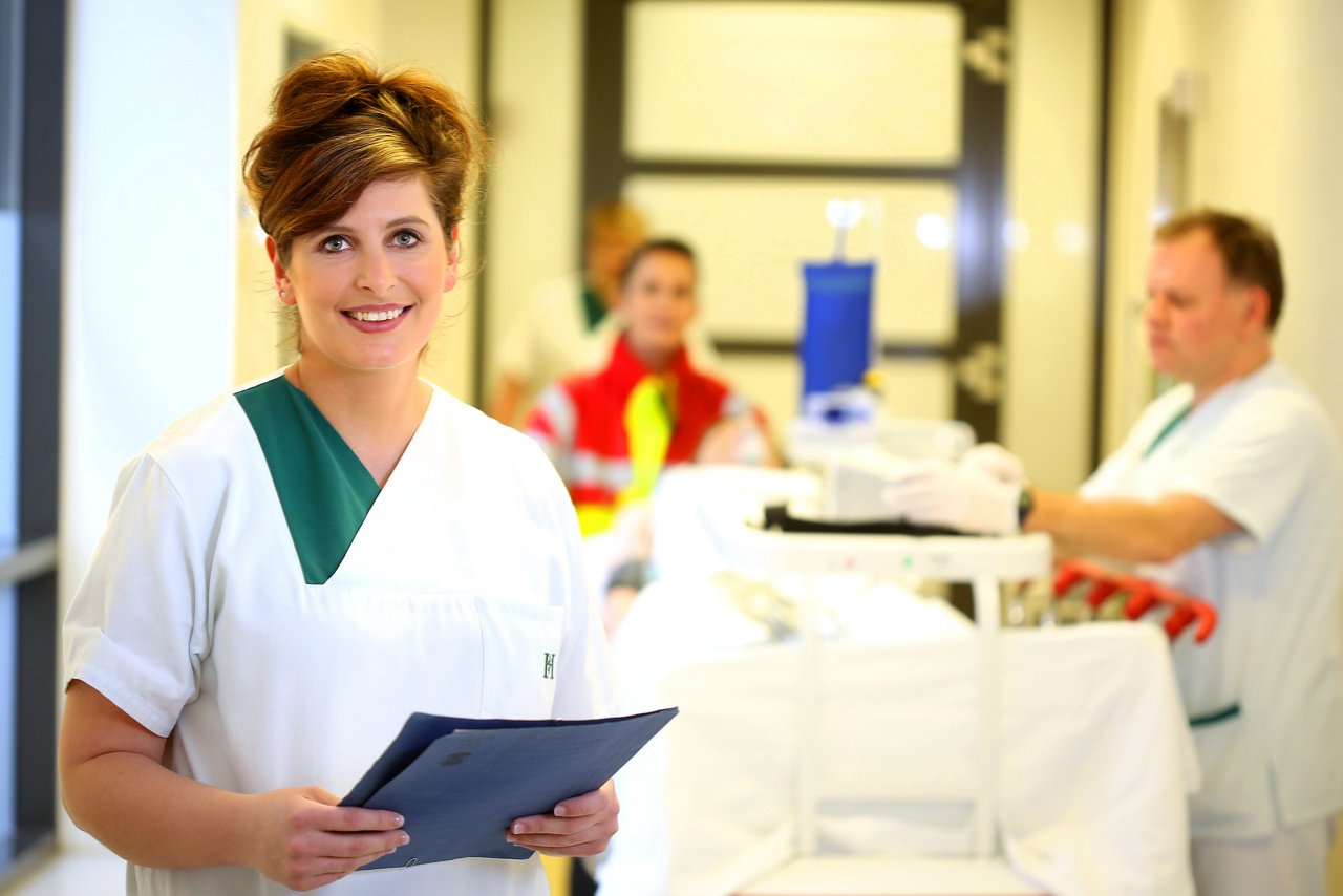 Pflegeschwester auf dem Stationsflur der ZNA  mit Rettungssanitäter und Notfallpatient im Hintergrund