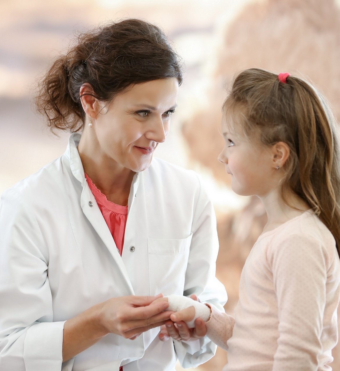 Ärztin spricht mit kleinem Mädchen, das einen Verband an der Hand hat