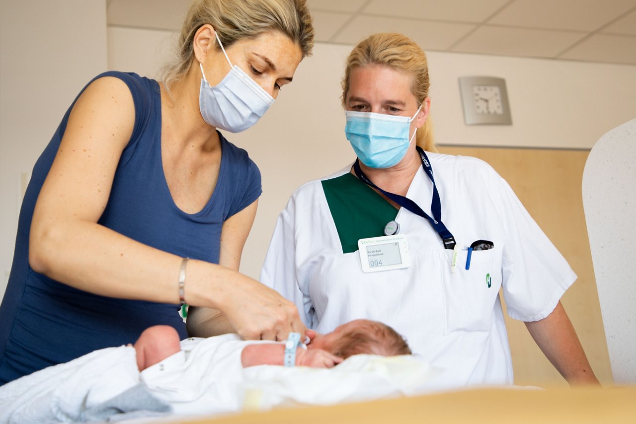 Mama zieht ihr Baby an und wird von Schwester unterstützt.